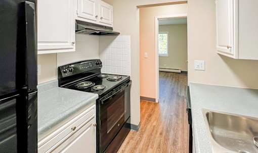A kitchen with a black fridge, black stove, and white cabinets at The Hampton Meadows Apartments,Des Moines