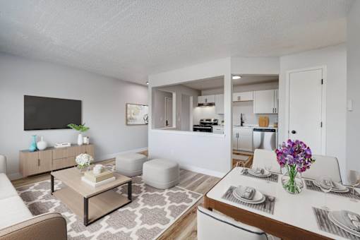 A modern living room with a white sofa, a coffee table, and a dining table set for two at The Hampton Meadows Apartments, Iowa, 50315