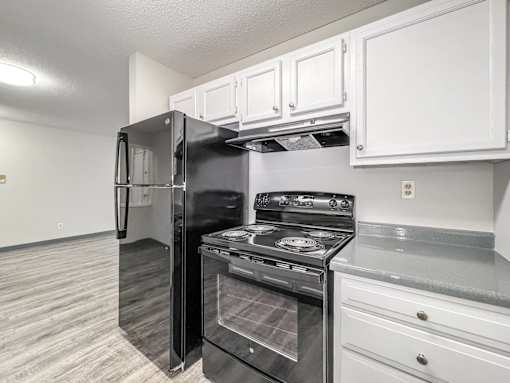 A black refrigerator and stove in a kitchen with white cabinets at The Ridges Apartments, Des Moines
