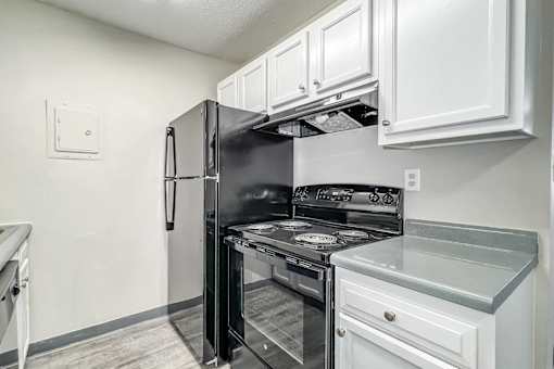 A black refrigerator is in a kitchen with white cabinets at The Ridges Apartments, Des Moines