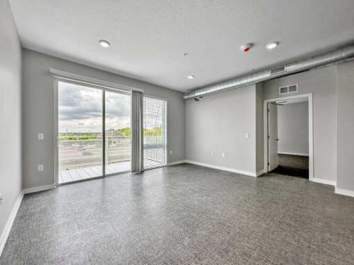 A spacious room with grey carpeting and a view of the outdoors through large windows.at Level, Des Moines Iowa   