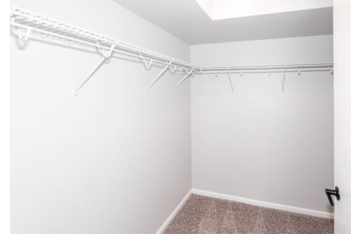an empty closet with white walls and a white closet with a hanging rack at Meadowlark Place Apartments, Grimes, IA,  50111