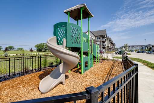 A playground with a green slide and a black fence.
