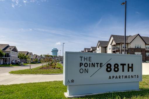 A sign for The Pointe on 88th Apartments in front of a grassy area and buildings.