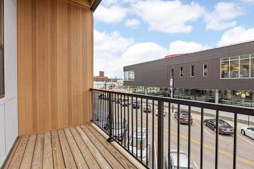 A balcony with a wooden floor and a black railing overlooking a street with cars.