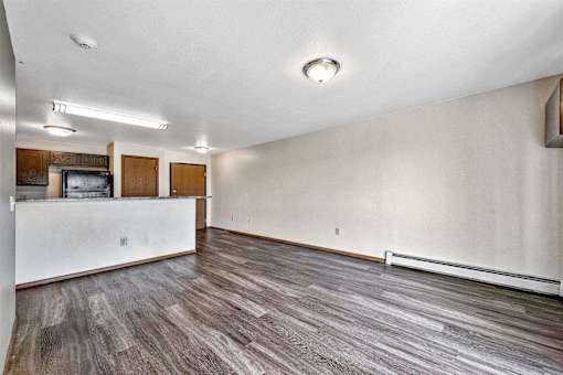 an empty living room with a white wall and wood flooring at Autumn Park, Sioux Falls, SD  