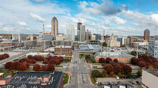 A cityscape with a mix of modern and older buildings, a parking lot, and trees with autumn foliage.
