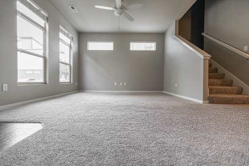 A spacious room with a carpeted floor and a staircase on the right side.