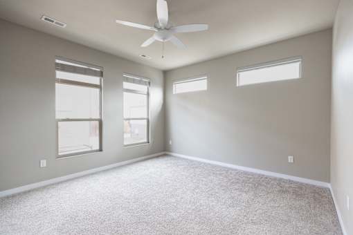 A spacious room with a ceiling fan and three windows.