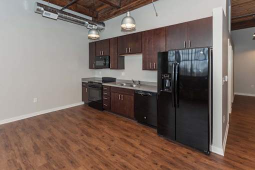 A black refrigerator is in a kitchen with wooden floors at Spaulding Lofts Apartments, Grinnell