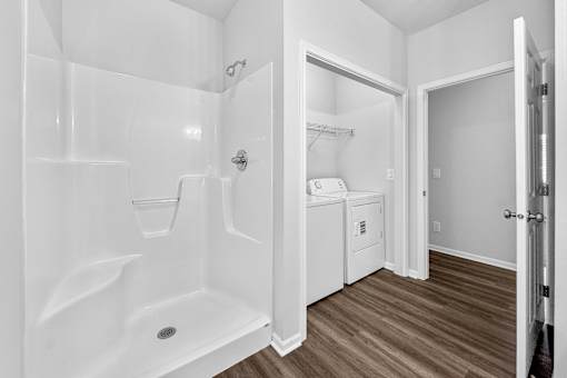 A white bathroom with a walk-in shower and a washer and dryer in the corner.