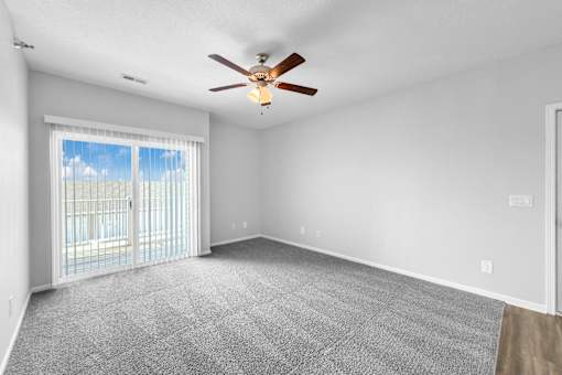 A spacious room with a ceiling fan and sliding glass doors leading to a balcony.