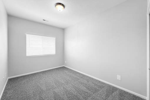 A room with a carpeted floor and a window with blinds.