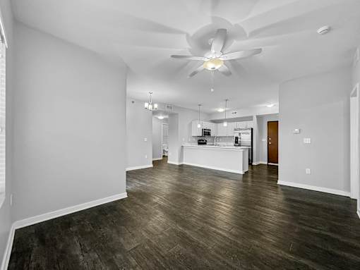 an empty living room with a ceiling fan and a kitchen at Stonegate Crossing Apartments, IOWA