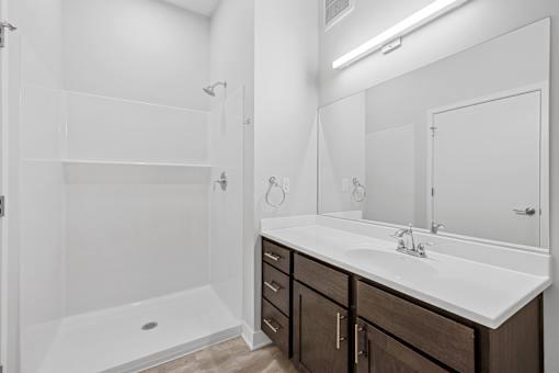 A white bathroom with a sink, mirror, and shower.