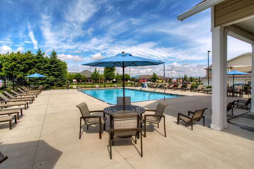 a swimming pool with a table and chairs under an umbrella at The Winhall of Williams Pointe Apartments, IOWA