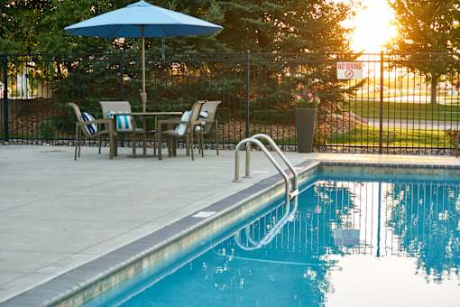 a swimming pool with an umbrella and a table with chairs at The Winhall of Williams Pointe Apartments, Waukee, IOWA