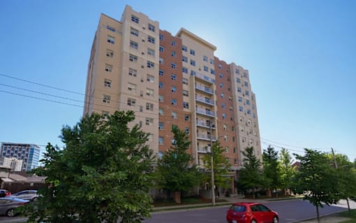 A red car is parked on the street in front of a tall apartment building.
