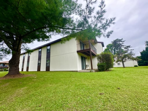 a white building with a green lawn and a tree
