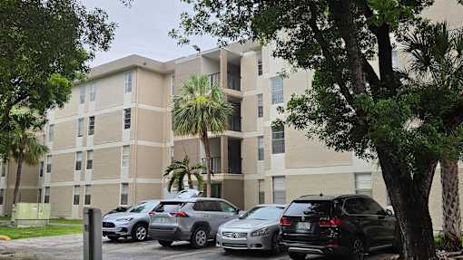 A parking lot with cars and a building with palm trees in front.