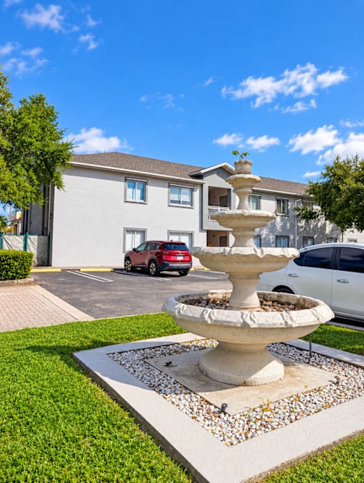 A white fountain in the middle of a grassy area in front of a building.