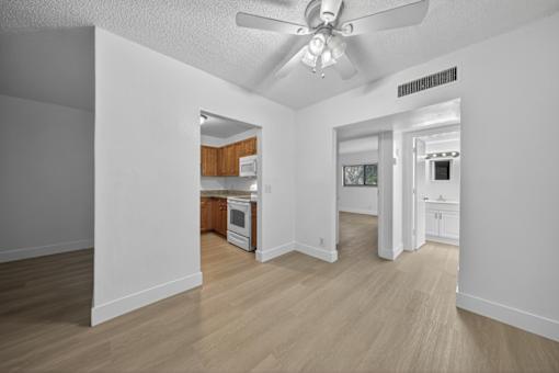 A room with a ceiling fan and a kitchen area in the background.