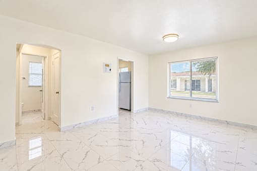 A spacious room with marble flooring and a window overlooking a building.
