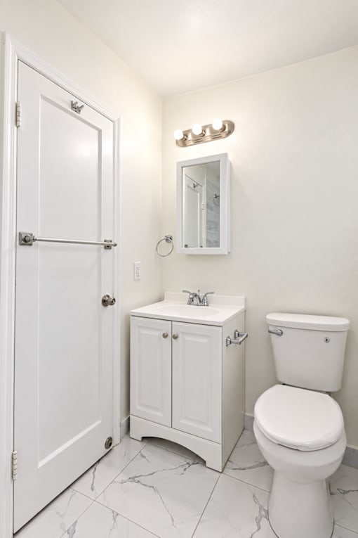 A white bathroom with a toilet, sink and medicine cabinet.