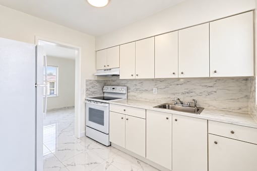 A kitchen with white cabinets and marble countertops.
