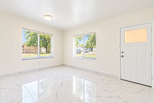 A room with a white door and windows with a view of the outside.