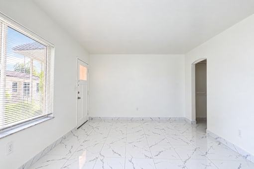 A room with white walls and marble flooring with a window on the left.