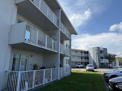 A white apartment building with balconies and cars parked in the background.
