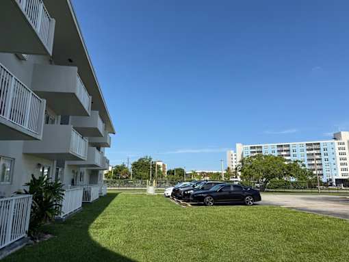 A black car is parked in a parking lot in front of a white building.