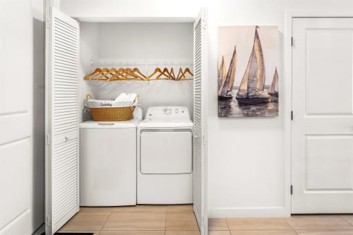 A laundry room with washer and dryer and a painting of a sailboat