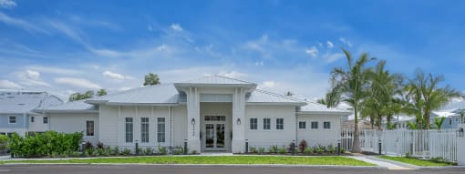 The front of a white house with a lawn and palm trees