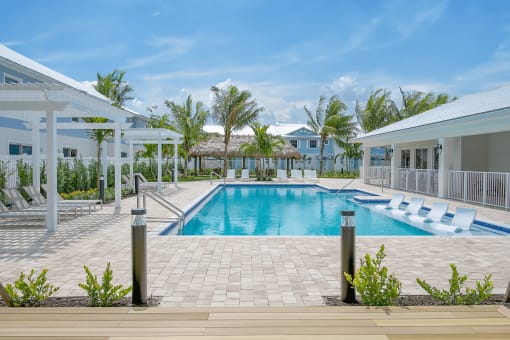 A swimming pool in front of a resort with white buildings