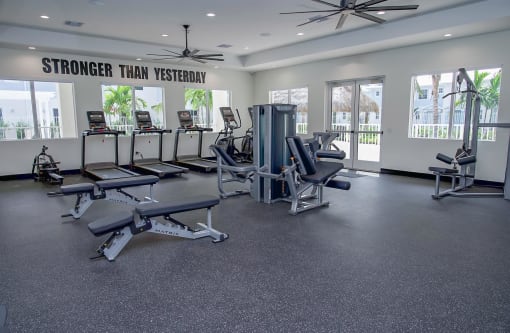 A gym with cardio equipment and weights in a building with windows