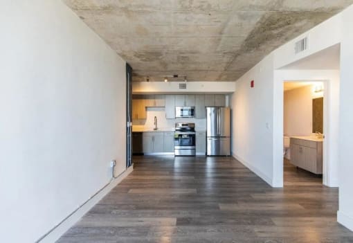 an empty living room with a kitchen in the background