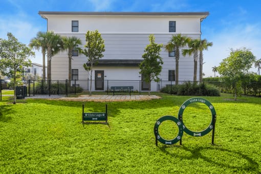 a white building with palm trees and a green lawn with a sign in the grass