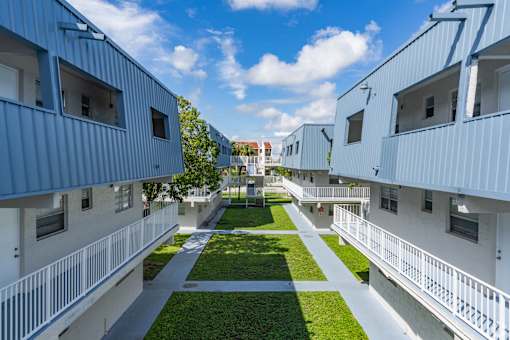 A row of white and blue buildings with green lawns in between.