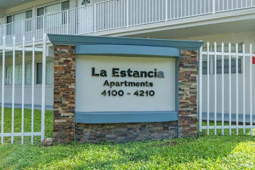 A sign for La Estancia Apartments is in front of a building.