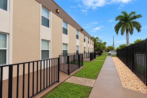 A long building with a black fence and a palm tree in the background.
