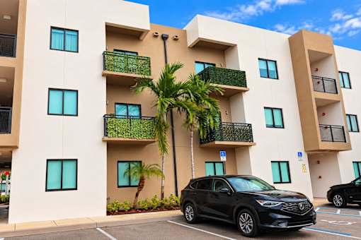 A black SUV is parked in a parking lot in front of a tan building with balconies.