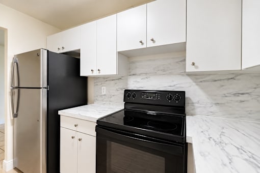 A black oven sits on a marble countertop in a kitchen with white cabinets.