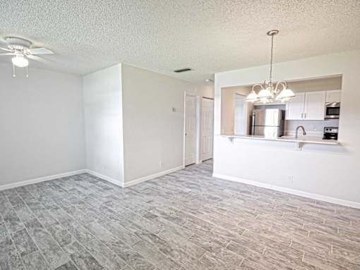 an empty living room with a kitchen and a ceiling fan