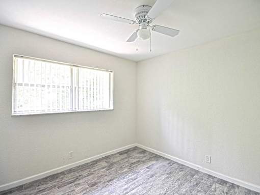 an empty bedroom with a ceiling fan and a window