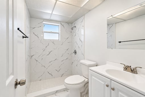 A white bathroom with a marble patterned shower.