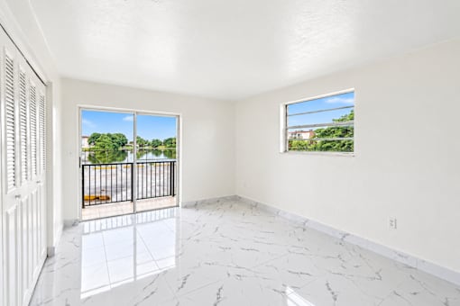 A room with a marble floor and a view of a fence and trees outside through the window.