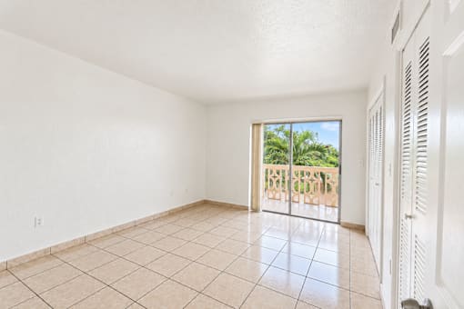 A room with a sliding glass door leading to a balcony with a view of trees.