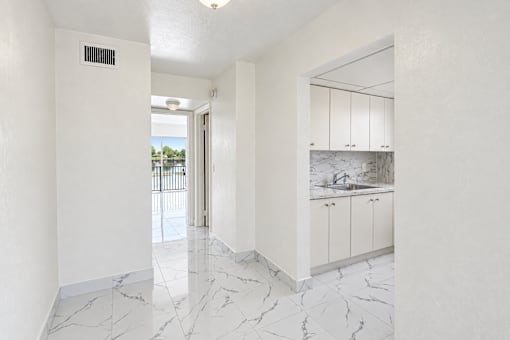 A white room with marble flooring and a kitchen area with white cabinets.